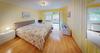 Foto vom Schlafzimmer. Heller Eichenboden, gelbe Wände und ein großes Doppelbett