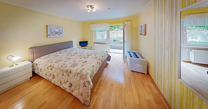 Foto vom Schlafzimmer. Heller Eichenboden, gelbe Wände und ein großes Doppelbett